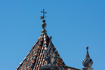 Old colored roof tiles with a vane, a cross and ornaments in Coimbra, Portugal.