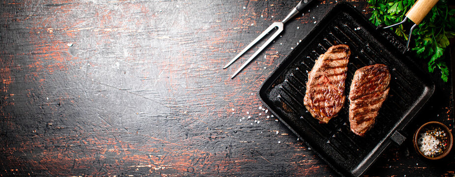 Aromatic grilled steak in a frying pan. Against a dark background. High quality photo
