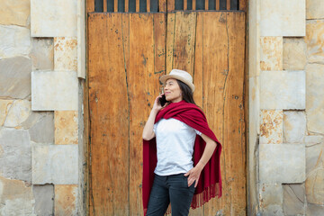 Latin woman wearing hat and a red shawl while talking on the phone with an old wooden door in the background