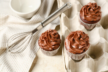 Tasty chocolate cupcakes with whisk on table in kitchen