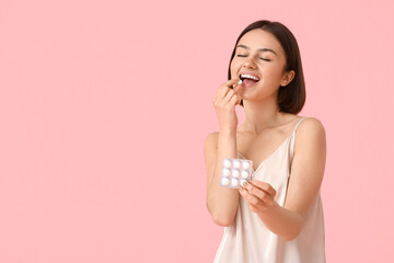 Young woman in pajamas and with chewing gum on color background