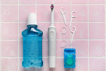 Dental floss with toothpicks, electric brush and rinse on pink tile background