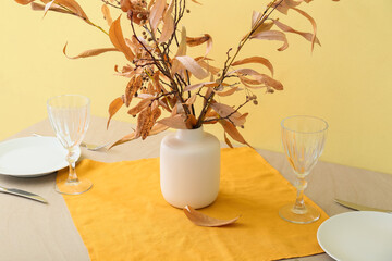 Beautiful table setting and vase with autumn decor near color wall, closeup