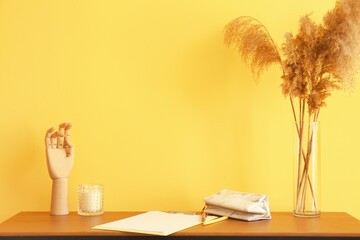 Workplace with stationery supplies, reed flowers and wooden mannequin hand near color wall