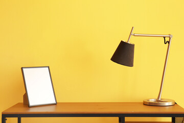 Workplace with modern lamp and blank photo frame near color wall