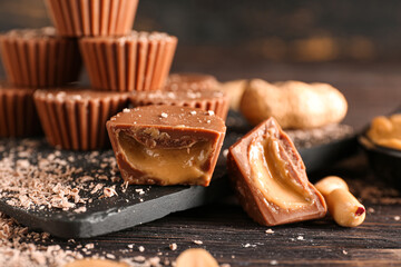 Board with tasty chocolate candies with peanut butter on dark wooden background, closeup