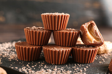 Board with tasty chocolate candies with peanut butter on dark wooden background, closeup