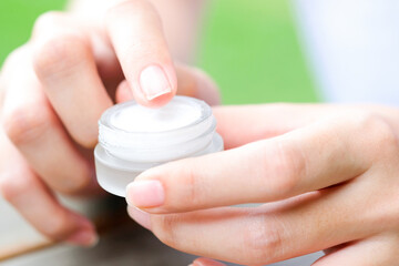 Hand of woman holding moisturizer cream and serum. She applying a facial cream , essential , oil , lotion and body cream for skin care, close up view and blur background. Beauty and Healthy Concept.