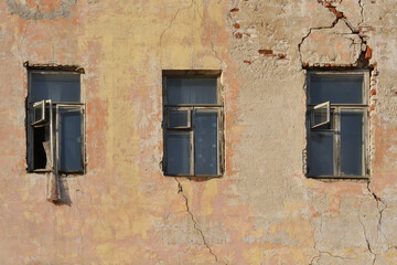Three rotten windows in the yellow plastered wall of a ruined old brick house
