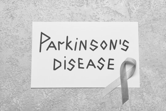 Paper sheet with text PARKINSON'S DISEASE and awareness ribbon on grunge background