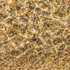A background of sand, small pebbles and flowing waves on the sea beach. Summer vacation concept