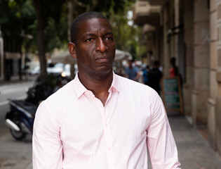 Fototapeta premium Closeup face of focused adult African American man walking along city street in summer day