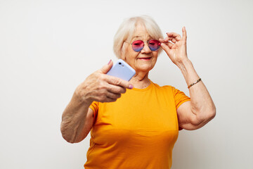 Portrait of an old friendly woman in a yellow t-shirt posing communication by phone cropped view