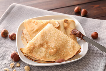 Plate of tasty thin pancakes with chocolate paste and nuts on table