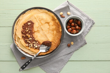 Plate of tasty thin pancakes with chocolate paste and nuts on green wooden background
