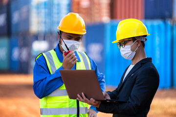 An Asian businessman in a black suit holds a laptop to inspect a container yard.