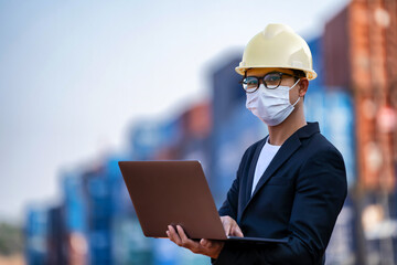 An Asian businessman in a black suit holds a laptop to inspect a container yard.