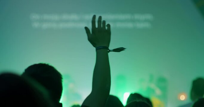 Christians Worship and Praise on Youth Festival or Conference. Unrecognizable People with Raised Arms on Music Live Concert or Show Event with Lights. 4K back view handheld shot in slow motion