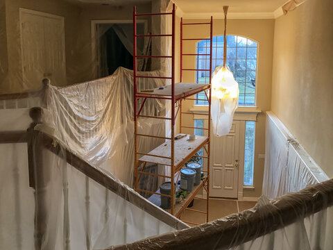 Two story residential home interior renovation work under construction. Drywall and ceiling painting project. Staircase and walls protected with plastic coverings.  