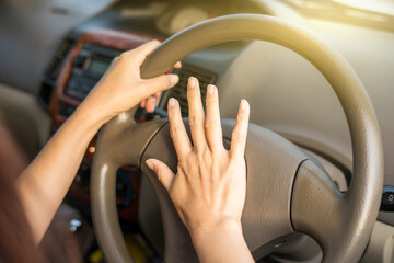 Hand female on the steering wheel of a car while driving the windshield and road. Close up of woman hand presses the horn on the steering wheel on her car.