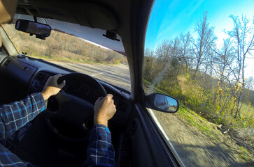 View from the interior of the car on the hands and steering wheel. The car is driving on an autumn road. Travel concept.