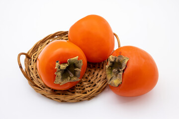 Ripe orange persimmon fruits in wicker basket. Isolated on white background.