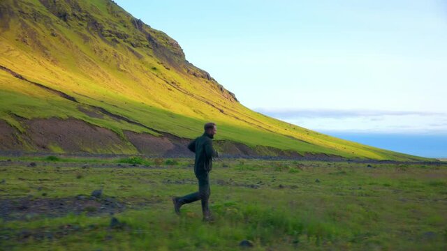 Caucasian Man Running On Grassy Terrain Near The Mountains Of Seljavallalaug In Southern Iceland. Tracking
