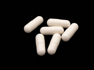 Pile of white capsules with medicine isolated on black background