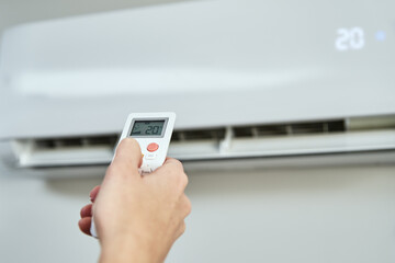 Hand adjusting temperature on air conditioner with remote control, Working air conditioner for...