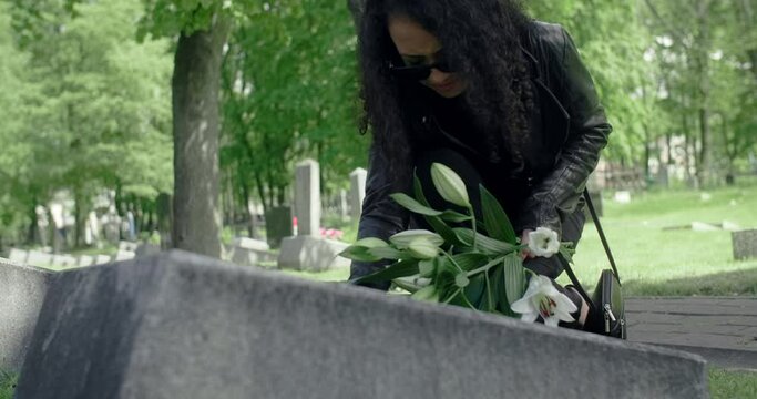 Black woman lays flowers to the grave stone and strokes it. Griving at the cemetery, 4k 60p Prores