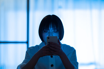 厳しい表情でスマートフォンを見つめる女性