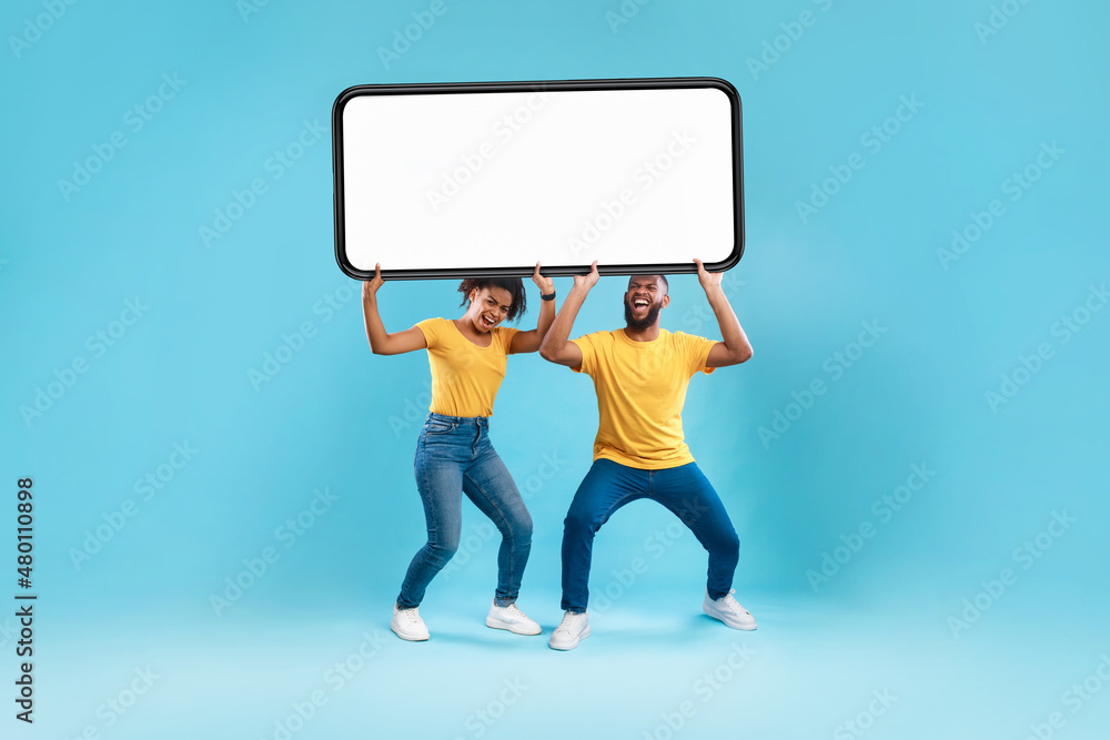 Poster black couple holding huge heavy smartphone with empty screen on blue background. mockup for ad, mobi