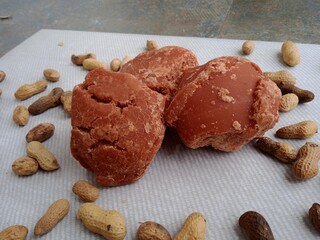 Red jaggery three pieces with peanuts in background. Jaggery is a natural sweetener also used to make brown sugar. 