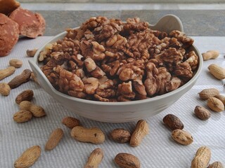 Close up of a bowl full of walnut kernels with peanuts on background and jaggery. Protein rich foods. Brain capacity increasing foods. 