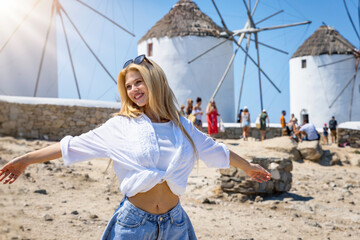 A happy tourist woman in front of the famous windmills of Mykonos island, Greece, during summer time - obrazy, fototapety, plakaty