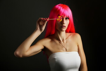 close up portrait of beautiful young woman with pink hairs holding lollipop on black background. 