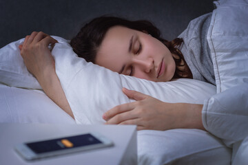 woman sleeping in bed early in the morning, the alarm clock on the smartphone is ringing