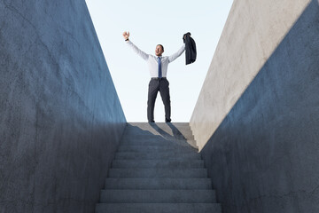 Happy european man celebrating success on top of abstract concrete stairs with sunlight. Growth and leadership concept.