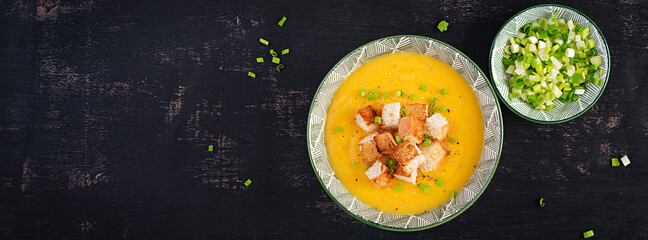 Creamy pumpkin puree soup with croutons, peppers and green onions. Top view, banner