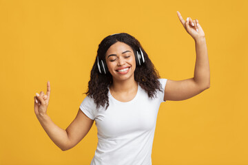 Move your body. Positive african american woman listening to music in wireless headphones and dancing, yellow background