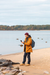 Caucasian man with smartphone in his hand standing in front of lake. A man catching a cellular network on a smartphone while walking