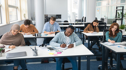 Diverse group of students sitting at desk writing in classroom