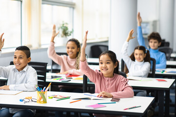 Fototapeta Diverse group of small schoolchildren raising hands at classroom obraz