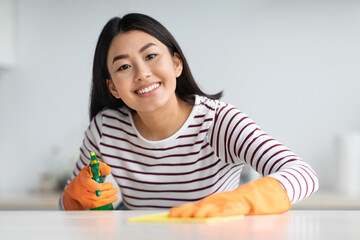 Cheerful asian woman house-keeper cleaning tables and smiling