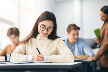 Smiling woman sitting at desk in classroom writing exam