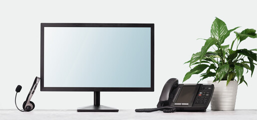 Computer monitor mockup for your design and VOIP headset phone on desk at modern office. Contemporary workplace or call centre operator with PC and headphones. Telecommunications support