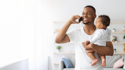 Black Man Holding Little Infant Child In Hands And Talking On Cellphone