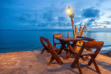 Cafe on a tropical beach, wooden table and chairs overlooking the sea and sunset