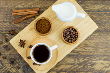 a cup of aromatic coffee on a wooden tray with a milkman, cinnamon sticks, coffee beans. coffee composition. top view.