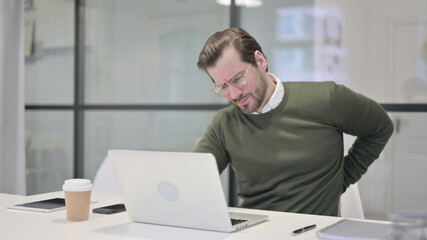 Young Businessman having Back Pain while using Laptop in Office